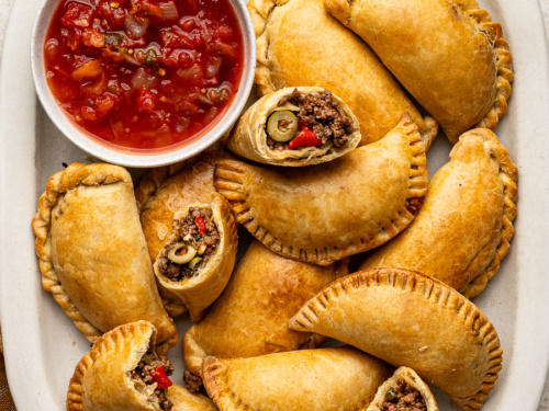 Baked empanadas on a wooden plate with cilantro garnish